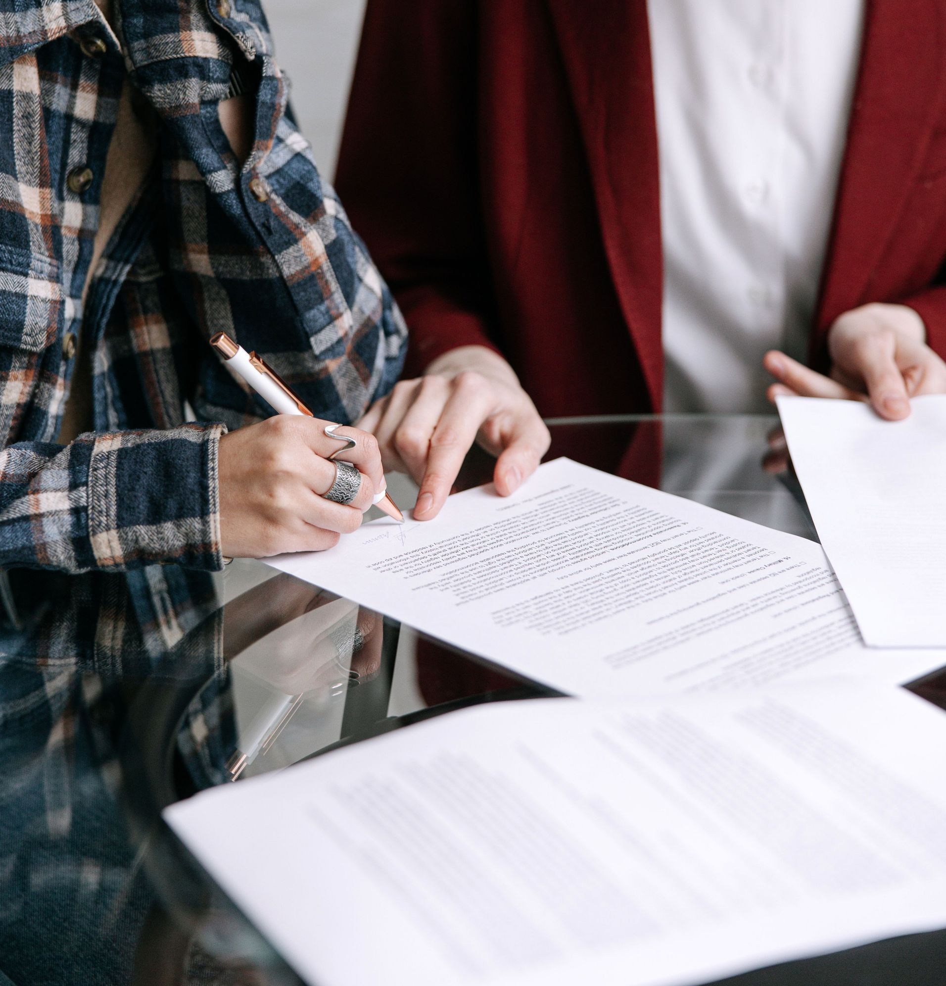 Two women reviewing and signing documents together at a glass table indoors.